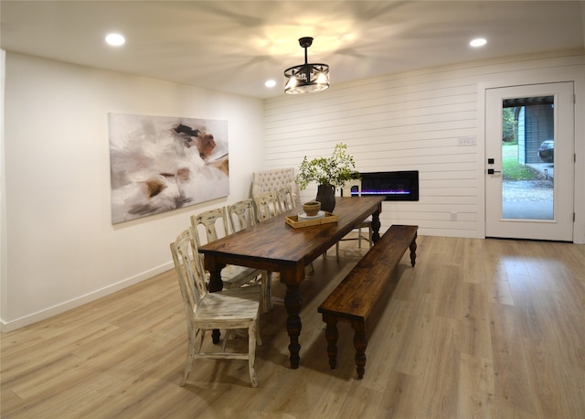 dining room featuring light hardwood / wood-style flooring, wooden walls, and a chandelier