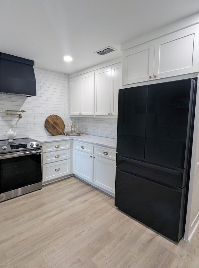 kitchen featuring light hardwood / wood-style floors, white cabinetry, ventilation hood, black fridge, and stainless steel range