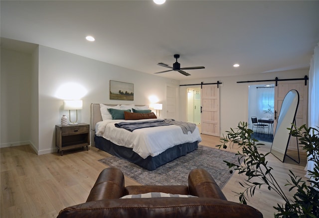 bedroom featuring ceiling fan, light hardwood / wood-style floors, and a barn door