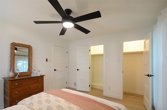 bedroom with a closet, ceiling fan, a walk in closet, and light hardwood / wood-style flooring