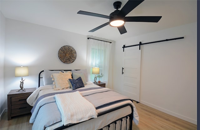 bedroom featuring ceiling fan, light hardwood / wood-style flooring, and a barn door