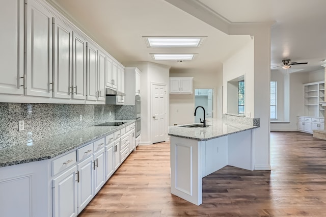 kitchen featuring white cabinetry, light stone counters, kitchen peninsula, ceiling fan, and sink