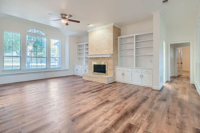 unfurnished living room with ceiling fan, built in shelves, light hardwood / wood-style flooring, a fireplace, and crown molding