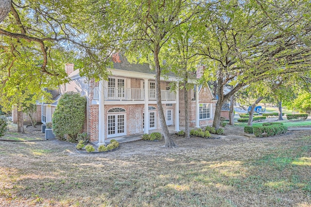 view of front facade with french doors, cooling unit, a balcony, and a front yard