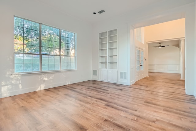 empty room featuring light wood-type flooring, built in shelves, and ceiling fan