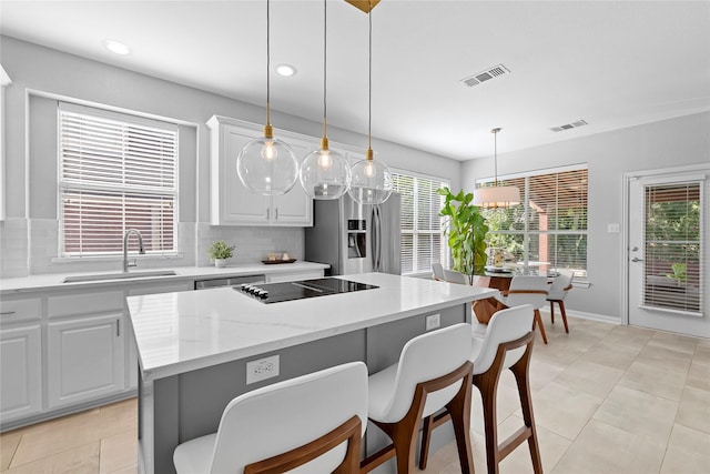 kitchen with sink, decorative light fixtures, backsplash, stainless steel refrigerator with ice dispenser, and a kitchen island