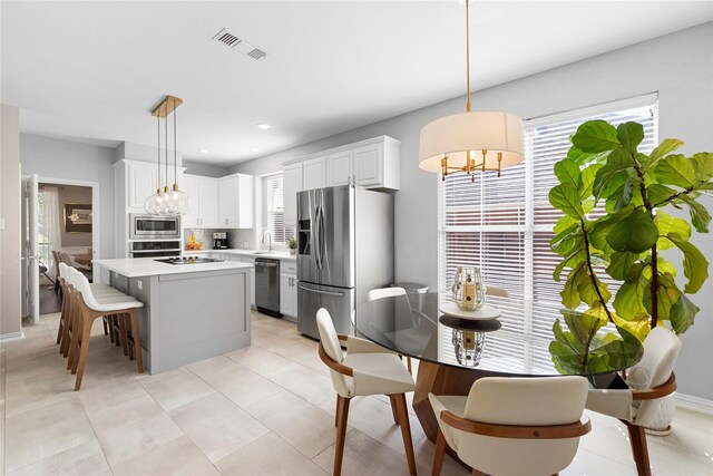 kitchen with appliances with stainless steel finishes, hanging light fixtures, a kitchen island, white cabinets, and sink