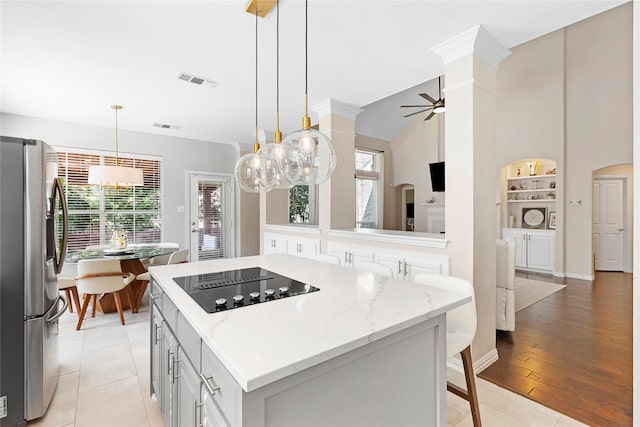 kitchen featuring light stone counters, a center island, black electric cooktop, stainless steel refrigerator, and ceiling fan