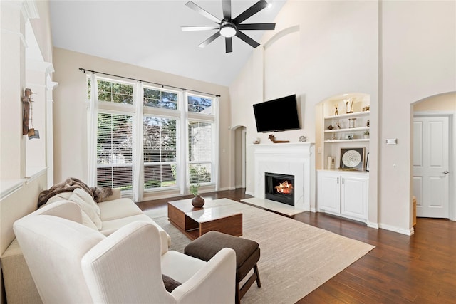 living room with high vaulted ceiling, dark hardwood / wood-style flooring, a high end fireplace, built in features, and ceiling fan