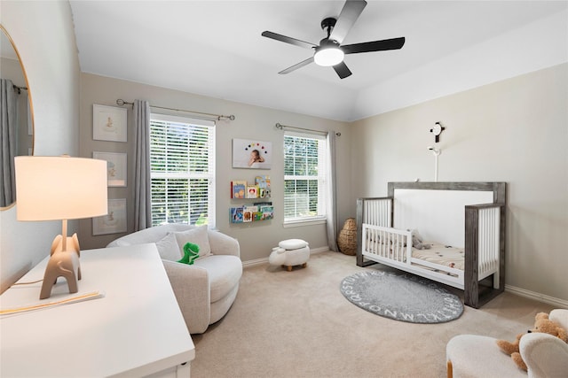 carpeted bedroom featuring a raised ceiling, ceiling fan, and a crib