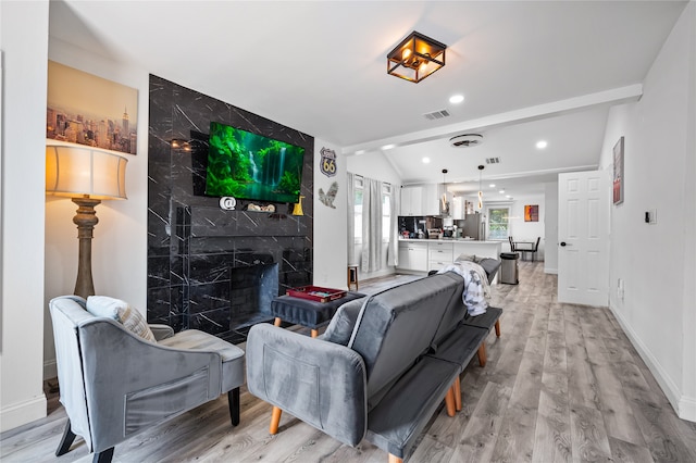 living room with light hardwood / wood-style flooring, tile walls, a high end fireplace, and vaulted ceiling