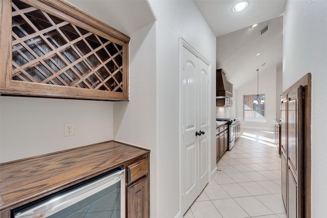 bar featuring an inviting chandelier, hanging light fixtures, vaulted ceiling, stainless steel gas stove, and light tile patterned floors