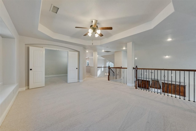 spare room with ceiling fan, a raised ceiling, and light carpet