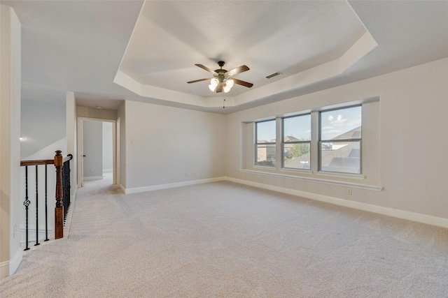 unfurnished room featuring light carpet, a tray ceiling, and ceiling fan