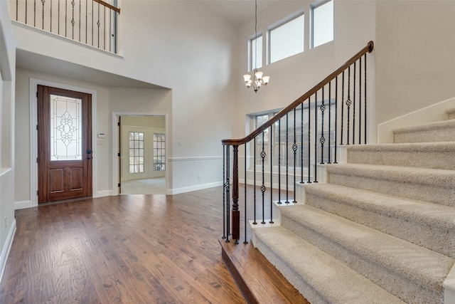 entryway with a chandelier, wood-type flooring, and a towering ceiling