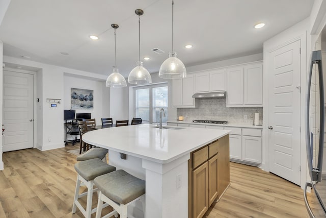 kitchen featuring white cabinetry, an island with sink, pendant lighting, light wood-type flooring, and sink