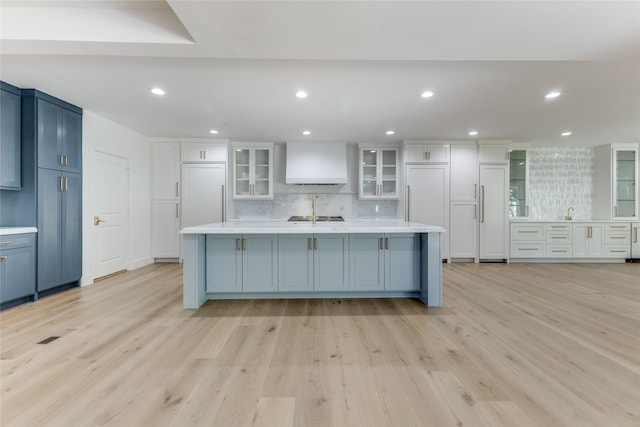 kitchen featuring decorative backsplash, light hardwood / wood-style floors, paneled fridge, and a large island with sink