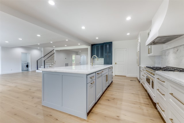 kitchen with a kitchen island with sink, washer / clothes dryer, custom range hood, light wood-type flooring, and high quality appliances