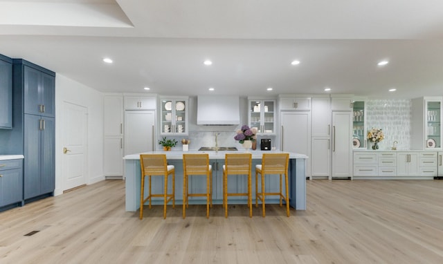 kitchen with a large island with sink, light wood-type flooring, a kitchen bar, and decorative backsplash