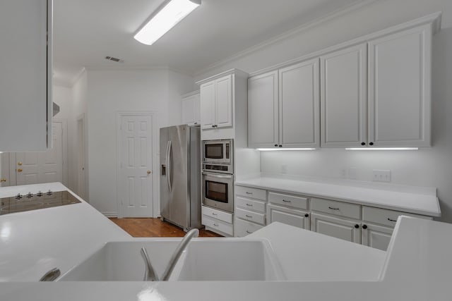 kitchen featuring wood-type flooring, stainless steel appliances, crown molding, and white cabinetry