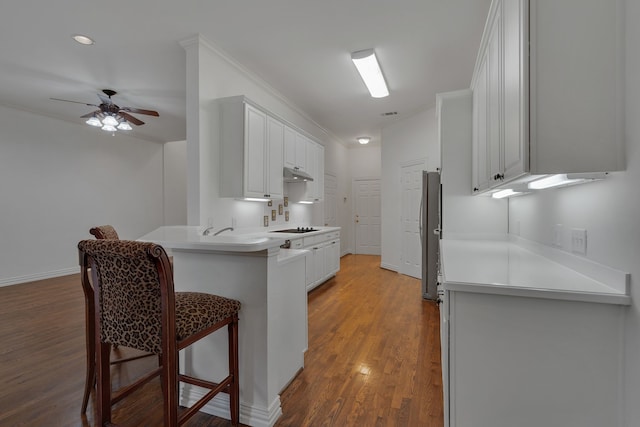 kitchen featuring black electric cooktop, a kitchen breakfast bar, dark wood-type flooring, white cabinets, and kitchen peninsula