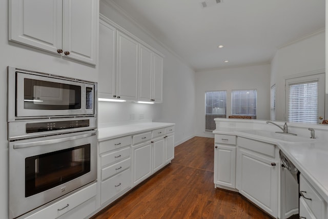 kitchen featuring appliances with stainless steel finishes, white cabinetry, dark hardwood / wood-style flooring, ornamental molding, and sink