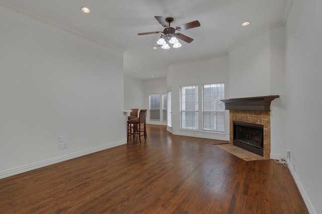 unfurnished living room featuring ornamental molding, a tiled fireplace, ceiling fan, and dark hardwood / wood-style floors