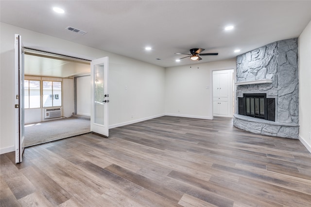 unfurnished living room with ceiling fan, a stone fireplace, wood-type flooring, and a wall mounted AC