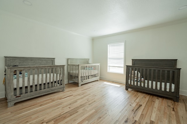 bedroom featuring a crib, light hardwood / wood-style flooring, and crown molding