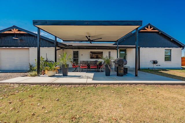 rear view of property featuring a lawn, a garage, ceiling fan, and a patio area