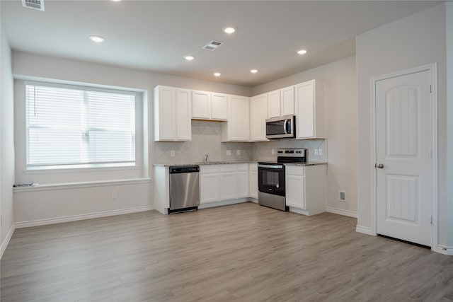 kitchen featuring tasteful backsplash, appliances with stainless steel finishes, white cabinetry, light stone counters, and light hardwood / wood-style flooring