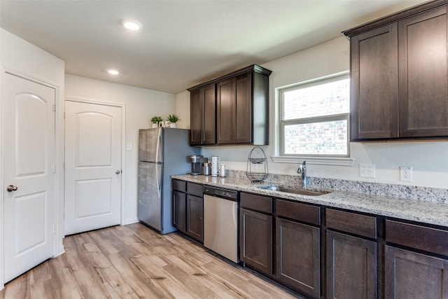 kitchen with sink, dark brown cabinetry, light wood-type flooring, appliances with stainless steel finishes, and light stone counters