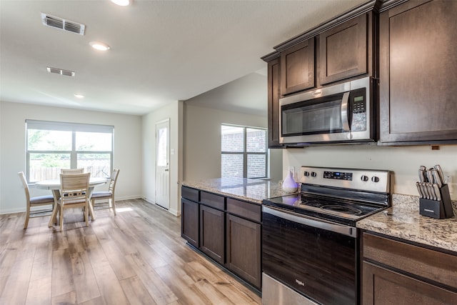 kitchen with appliances with stainless steel finishes, light stone countertops, dark brown cabinets, and light hardwood / wood-style floors