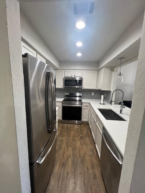 kitchen featuring pendant lighting, sink, backsplash, white cabinetry, and appliances with stainless steel finishes