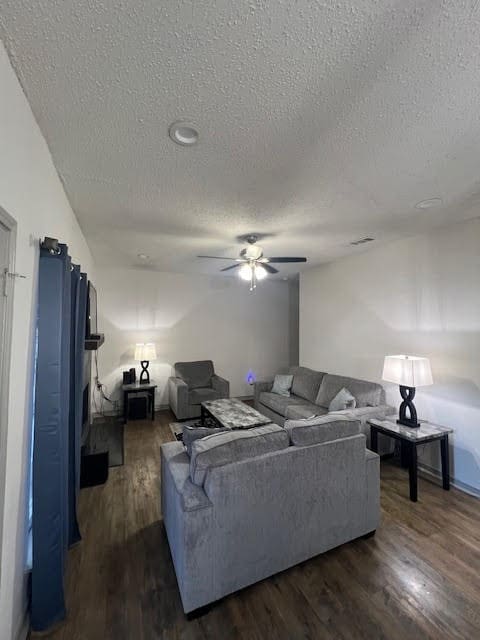 living room featuring ceiling fan, a textured ceiling, and dark hardwood / wood-style floors