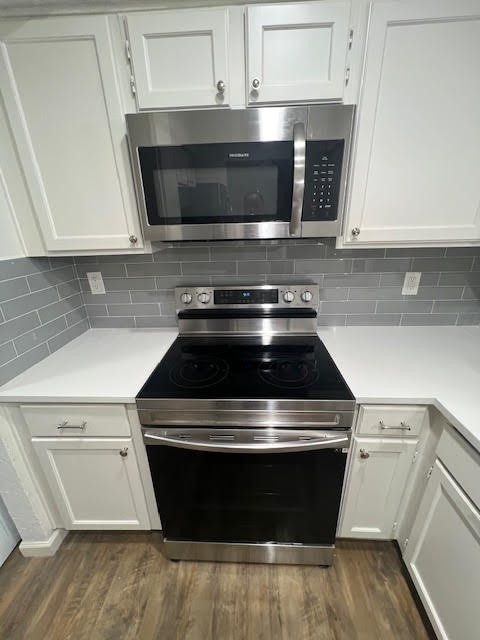 kitchen featuring backsplash, stainless steel appliances, white cabinetry, and dark hardwood / wood-style flooring