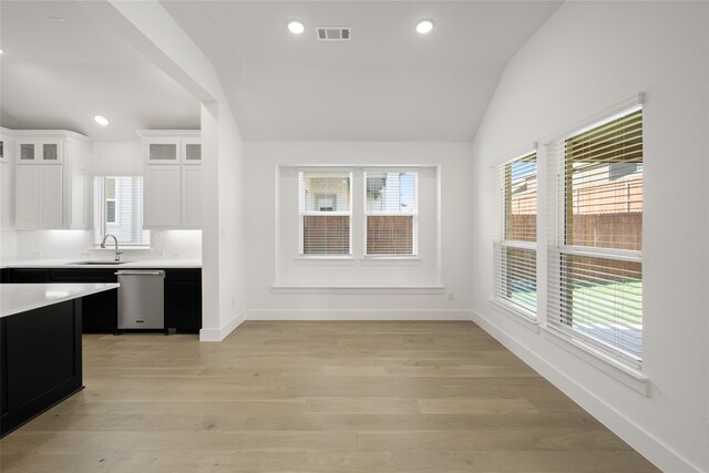 kitchen with white cabinetry, sink, stainless steel dishwasher, vaulted ceiling, and light wood-type flooring