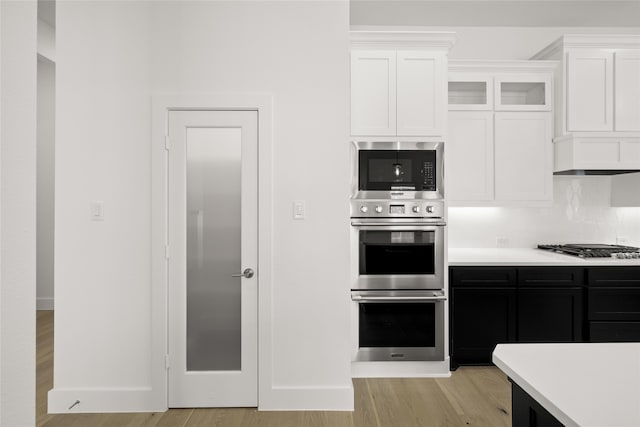 kitchen with decorative backsplash, white cabinetry, light wood-type flooring, and appliances with stainless steel finishes