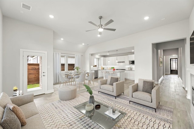 living room featuring light hardwood / wood-style floors, vaulted ceiling, and ceiling fan