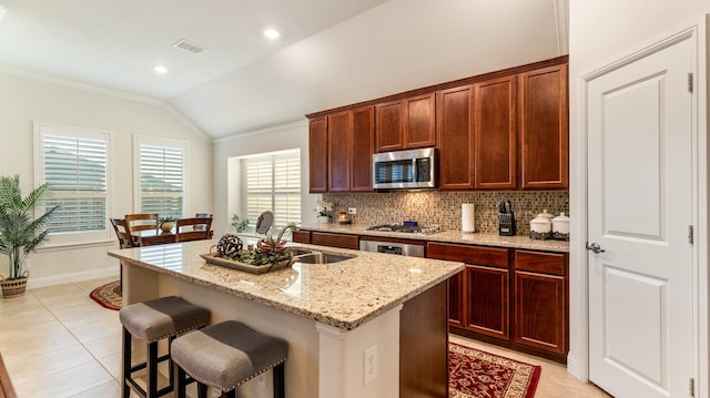 kitchen with light stone counters, lofted ceiling, sink, a center island with sink, and stainless steel appliances