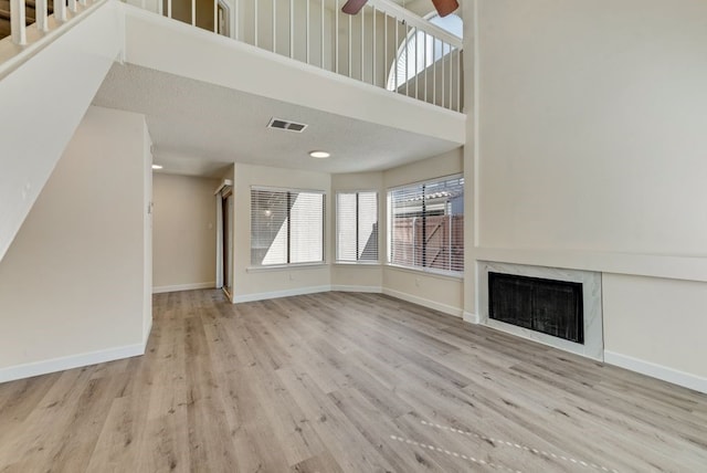 unfurnished living room featuring ceiling fan, a textured ceiling, a fireplace, and light hardwood / wood-style flooring