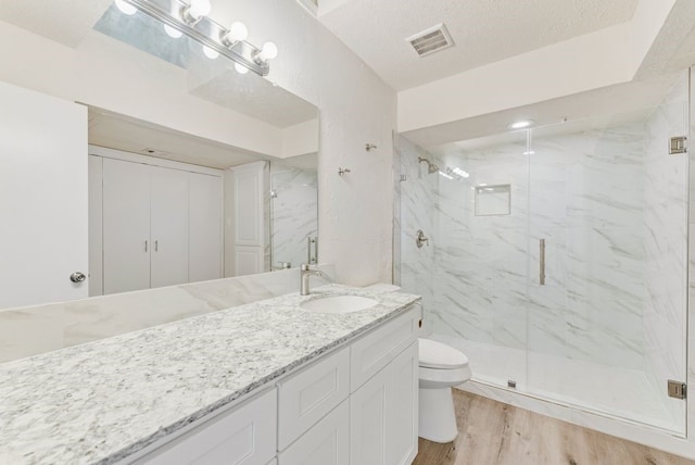 bathroom featuring a textured ceiling, hardwood / wood-style flooring, a shower with door, vanity, and toilet