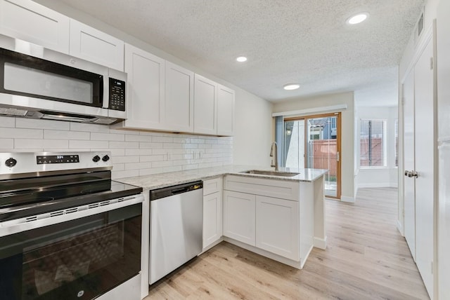 kitchen with appliances with stainless steel finishes, white cabinetry, light stone counters, kitchen peninsula, and sink