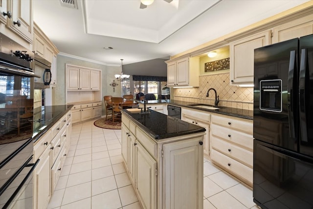 kitchen featuring black appliances, a kitchen island with sink, cream cabinetry, and decorative light fixtures