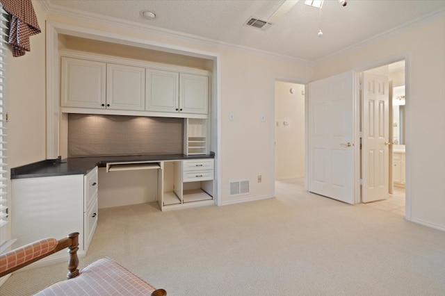 carpeted office space featuring a textured ceiling, built in desk, ceiling fan, and crown molding