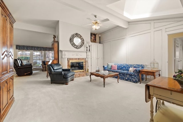 living room with a brick fireplace, light carpet, beam ceiling, and ceiling fan