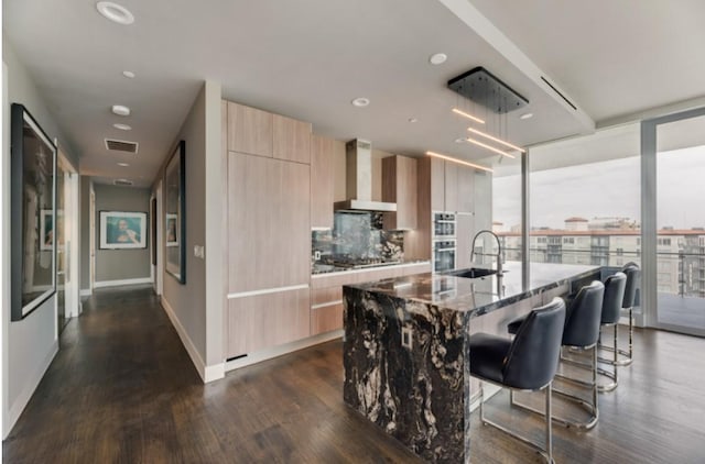 3130 N Harwood St Unit 1506, Dallas, TX 75201 - kitchen featuring light brown cabinetry, modern cabinets, dark stone countertops, wall chimney range hood, and visible vents
