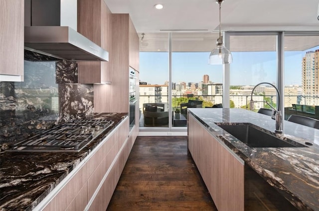 kitchen featuring dark stone counters, dark wood-type flooring, sink, ventilation hood, and decorative light fixtures