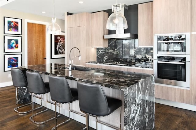 kitchen with hanging light fixtures, a breakfast bar area, light brown cabinetry, dark stone counters, and sink