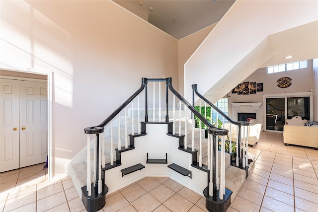 stairs featuring a towering ceiling, a high end fireplace, and tile patterned floors